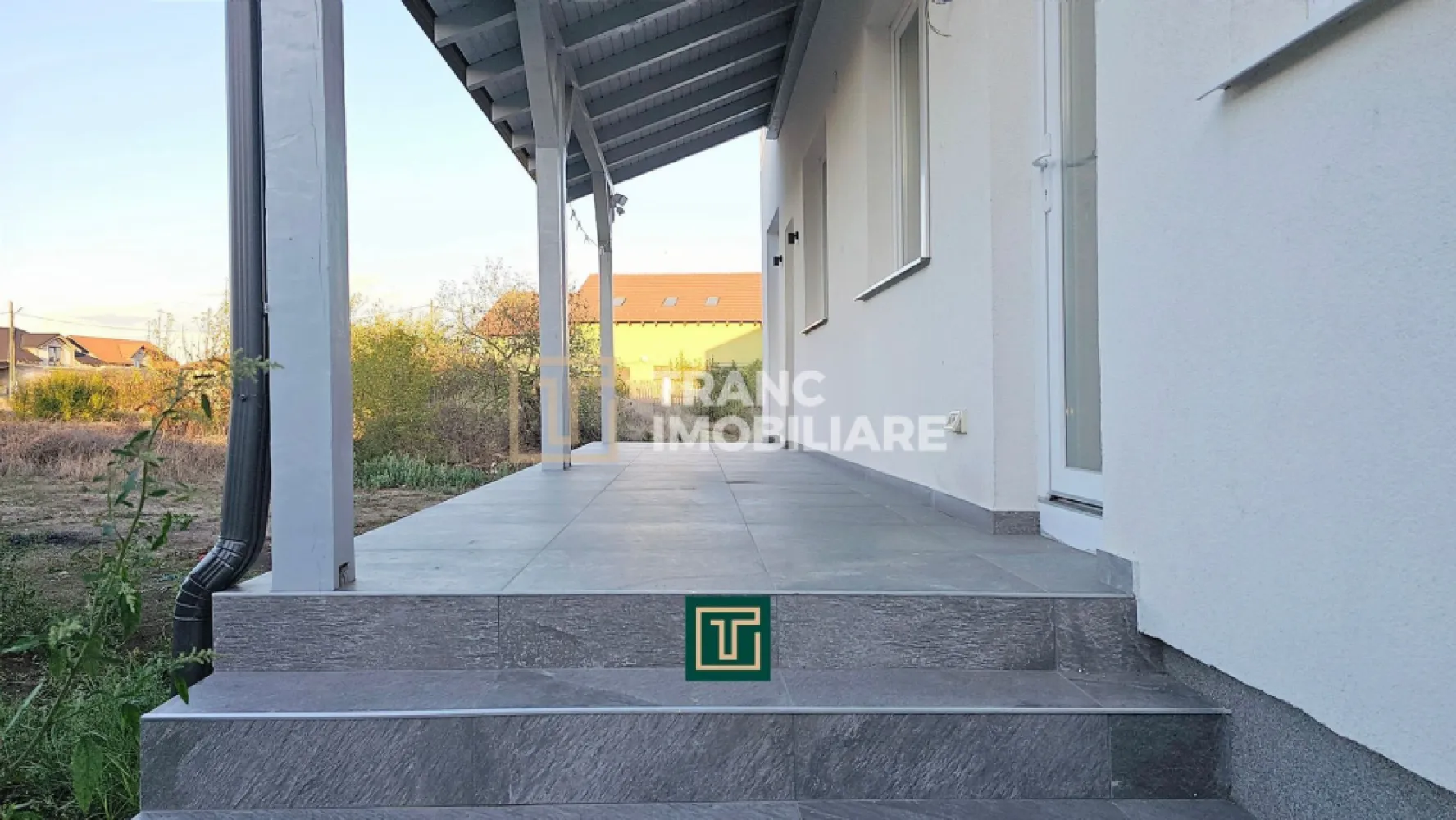 Jumătate de duplex nou cu 4 camere in Vladimirescu - În Vladimirescu, într-o zonă liniștită, dar cu acces rapid la centura Aradului, Tranc Imobiliare vă oferă la vânzare o locuinta formata din jumatate dintr-un duplex nou, finalizat în 2025 și pregătit să fie locuit imediat. Locuința se predă la cheie, nemobilată, cu finisaje moderne și de calitate superioara, gândite pentru a oferi un ambient elegant și ușor de personalizat de către viitorii proprietari.

Suprafața construită este de 154 mp, iar cea utilă de 96 mp, desfășurată pe parter, mansardă și pod. Terenul are 342 mp, cu un front stradal de 8 metri și acces direct din drum asfaltat. Compartimentarea este practică și bine gândită: living luminos, bucătărie spațioasă, trei dormitoare, două băi complet funcționale, o terasă acoperită de 7,6 mp, dar și o cameră tehnică situată sub scară, unde se află centrala termică și spațiu suplimentar pentru depozitare și mașina de spălat. În fața casei, proprietarii beneficiază de o parcare acoperită de 18 mp.
Finisajele interioare sunt moderne și luminoase, cu pardoseli din parchet și gresie în tonuri calde, pereți zugrăviți cu lavabil alb, plinte elegante, uși interioare albe cu design contemporan și băi complet amenajate cu faianță de bun gust. Totul este nou și pregătit pentru a fi folosit din prima zi.

Din punct de vedere tehnic, casa este solid construită, cu pereți din cărămidă, fundație de beton și acoperiș din țiglă ceramică. Izolația exterioară din polistiren de 10 cm asigură eficiență energetică, iar instalațiile electrice din cupru și cele sanitare din PPR oferă durabilitate. Încălzirea se realizează prin centrală pe gaz, cu incălzire în pardoseală. Proprietatea este racordată la toate utilitățile, apă, gaz, curent trifazic, canalizare.
Chiar dacă dormitoarele sunt mai compacte, avantajele acestei proprietăți, prin faptul că este o construcția nouă, finisajele sunt moderne, are eficiența energetică ridicată și zona este liniștită, dar totuși aproape de centură si de zona centrală a satului Vladimirescu, o transformă într-o alegere foarte bună atât pentru locuință permanentă, cât și ca investiție.

Curtea poate fi transformată într-o grădină verde, cu gazon, flori și arbori, sau într-un spațiu de relaxare cu foișor și loc de grătar. Pentru familiile cu copii, terenul poate deveni loc de joacă privat, iar pentru cei care apreciază confortul, există suficient spațiu pentru o piscină mică ori o zonă de terasă extinsă. Astfel, cumpărătorul nu achiziționează doar o locuință modernă, ci și libertatea de a-și crea propriul colț de liniște și confort după dorințe.

Această locuința este soluția ideală pentru o familie care își dorește o casă nouă, bine compartimentată și gata de locuit, unde tot ce rămâne de făcut este să fie mobilată și decorată după gustul personal.