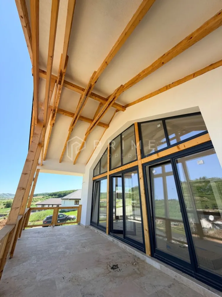 Vilă chalet modern cu perete panoramic de sticlă - Livezeni, Mureș - Vă prezentăm la vânzare o casă individuală cu design chalet contemporan, situată într-un cartier rezidențial aerisit din Livezeni, județul Mureș. Construcția impresionează prin peretele panoramic de sticlă pe toată înălțimea șarpantei, care inundă livingul cu lumină naturală și oferă o priveliște deschisă spre dealurile împrejmuitoare.
Planul interior se desfășoară pe un singur nivel, cu o configurație gândită pentru confort și funcționalitate: 
bucătărie cu living open-space, trei dormitoare generoase, două băi, dressing și cămară. 
Terasa acoperită de 25 m², cu balustradă din sticlă și lemn, prelungește natural spațiul de locuit spre exterior.
Podul este podit și poate fi utilizat ca spațiu de depozitare suplimentar, un avantaj rar în construcțiile noi.
Izolație superioară · eficiență energetică ridicată
Exterior termoizolat cu polistiren expandat de 15 cm; interior izolat cu spumă poliuretanică aplicată în strat continuu — eliminarea punților termice și consum redus de energie pe tot parcursul anului.
Proprietatea se vinde la stadiu finisat.

La Prime Properties, fiecare tranzacție înseamnă mai mult decât o simplă achiziție. Este un proces complet, în care colaborăm cu cei mai buni profesioniști: notari, avocați, designeri, arhitecți, evaluatori, specialiști în certificate energetice, consultanți de credite imobiliare.
Astfel, atunci când alegi o proprietate prin noi, primești la pachet și siguranță, transparență și servicii impecabile pe tot parcursul drumului tău către casa ideală.
Ne dedicăm 100% fiecărui client, iar asta se reflectă în rezultate și în încrederea pe care o primim înapoi prin recomandările lor.
Proprietatea aceasta nu se potrivește exact nevoilor tale?
Lasă-ne să îți găsim alternativa potrivită. Agentul nostru îți va oferi soluții avantajoase și adaptate stilului tău de viață.
📞 Contactează-ne astăzi. Până acum nu am dezamăgit niciun client și nu vom începe cu tine.
Comision 0% pentru cumpărători