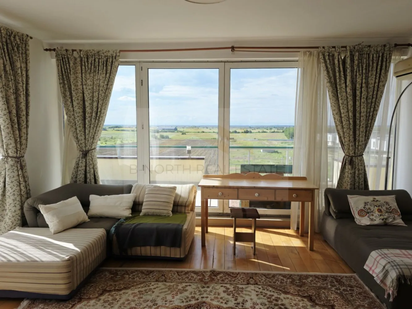 Penthouse 148mp cu terase75 mp și șemineu | Corbeanca - B-North Real Estate vă prezintă spre vânzare un penthouse cu suflet, view panoramic și terase generoase, situat în complexul rezidențial North Point Corbeanca, în Ostratu – un loc în care liniștea, natura și confortul se îmbină perfect cu accesul rapid către nordul Bucureștiului.
Sunt locuințe care se aleg pentru suprafață.
Și sunt locuințe care se simt din primul moment.
Acest penthouse face parte din a doua categorie: o locuință luminoasă, aerisită, cu spații generoase, șemineu, terase ample și o priveliște superbă, deschisă către natură. Este genul de apartament în care simți libertatea unei case, dar păstrezi confortul unui complex rezidențial închis.
Proprietatea este situată la etajul 4 al unui imobil cu lift și oferă o atmosferă rar întâlnită într-un apartament: multă lumină naturală, intimitate, vedere panoramică și zone de relaxare atât la interior, cât și la exterior.
Locuința dispune de aproximativ 148 mp interiori, completați de aproximativ 75 mp de terase, perfecte pentru cafeaua de dimineață, seri liniștite, plante, zonă de lounge sau mese în aer liber cu vedere deschisă.
Zona de zi este unul dintre cele mai frumoase puncte ale proprietății: living amplu, dining luminos, șemineu și acces către terase. Este un spațiu cald și primitor, potrivit pentru familie, seri cu prietenii sau momente de liniște acasă, departe de agitația orașului.
Se vinde mobilat și utilat, cu electrocasnice incluse, oferind o bază foarte bună pentru o locuință spectaculoasă, care poate fi ușor personalizată de viitorul proprietar.
Compartimentarea include:
living generos cu acces către terasă
zonă de dining cu vedere panoramică
bucătărie separată, mobilată și utilată
2 dormitoare,2 băi,spații de depozitare,șemineu,terase ample, cu priveliște deschisă,loc de parcare inclus
Complexul North Point Corbeanca este un complex rezidențial închis, cu acces securizat cu barieră, loc de joacă pentru copii, spații verzi și o frumoasă alee de platani la intrare. Atmosfera este una elegantă, aerisită și relaxată – ideală pentru familii, pentru persoane care lucrează de acasă sau pentru cei care își doresc să locuiască aproape de natură, dar nu izolați.
Poziționarea este un avantaj important. Deși te bucuri de liniște, aer curat și intimitate, ai acces rapid către punctele importante din nordul Capitalei:
aproximativ 10-15 minute până la Aeroportul Otopeni
aproximativ 10-15 minute până la Therme București
aproximativ 15-20 minute până la Băneasa Shopping City și zona comercială Băneasa
aproximativ 25-35 minute până în nordul Bucureștiului, în funcție de trafic
În apropiere se regăsesc supermarketuri, restaurante, grădinițe, școli, centre comerciale și zone de relaxare, păstrând în același timp sentimentul de retragere într-o zonă verde și liniștită.
Acest penthouse este o alegere excelentă pentru cei care caută mai mult decât un apartament: caută spațiu, lumină, terase, view, siguranță și o atmosferă de acasă.